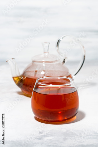 glass cup of tea and teapot on white background, closeup vertical