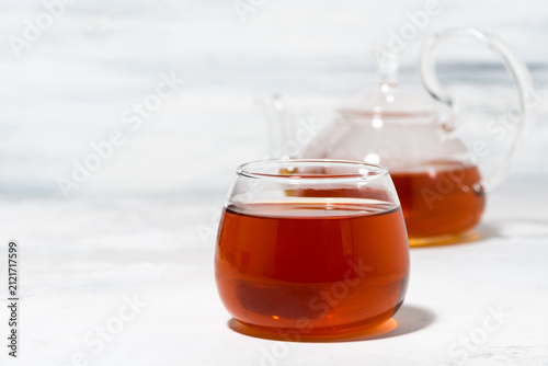 glass cup of tea and teapot on white background, closeup
