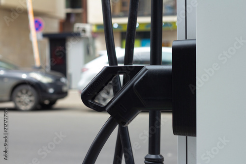 Horizontal street city photo close up. Black plug in socket on white electric car charging station on parking. Concept of alternative fuel, free energy, green power, zero waste, auto, earth day