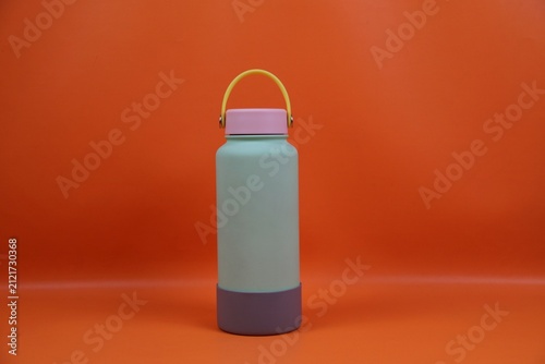 Pastel colored water bottle with a yellow handle and pink cap set against a orange background, conveying modern minimalism and portable hydration for everyday use.