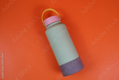 Pastel colored water bottle with a yellow handle and pink cap set against a orange background, conveying modern minimalism and portable hydration for everyday use.