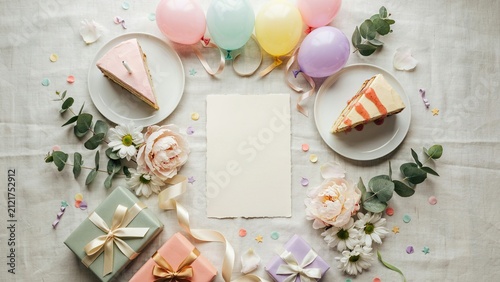 Cake slices served on ceramic plates sit beside a blank paper card surrounded by colorful balloons and gifts.