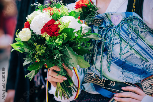 Villach, Austria - August 01, 2026: Woman in traditional attire holds a vibrant bouquet of flowers during the Villacher Kirchtag Parade, showcasing cultural heritage and festive spirit