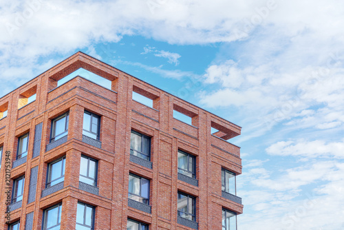 A red brick facade of a modern residential apartment building corner. A minimalist urban architecture design with extensive sky copy space.