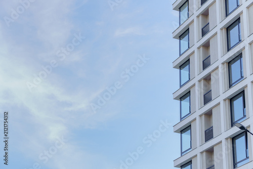 A modern residential building facade with geometric glass windows and a white concrete exterior. A contemporary urban apartment skyscraper corner with extensive sky copy space.
