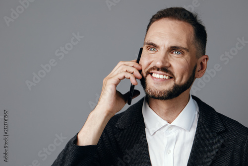 Foto Professional business man speaks on a phone against a colored isolated background, his confident smile and relaxed posture convey seriousness with approachability and strong leadership