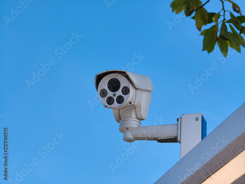 White security camera mounted on building exterior wall. Outdoor surveillance system for monitoring safety and crime prevention.