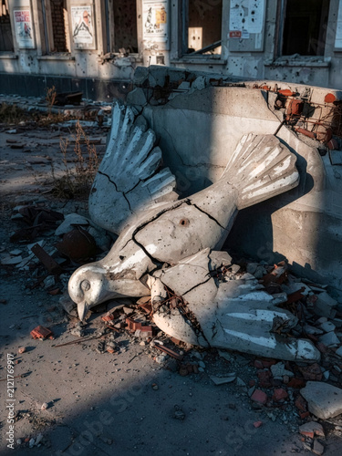 A shattered concrete dove lies amid the rubble of a war-damaged building. An anti-war symbol of broken peace, civilian suffering and the devastating consequences of armed conflict.