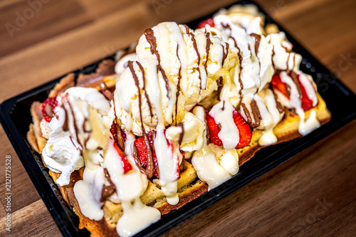 Freshly baked crepe and waffel with ice cream, chocolate and berries on wooden table. Served with spoon. Filled pancakes with strawberries, fresh berries and sauce.
