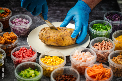 Baked potatoes with cheese, herbs, meat and butter. Copy space background. BBQ or steakhouse side dish favorite with tomato beans, cheddar cheese, bacon.