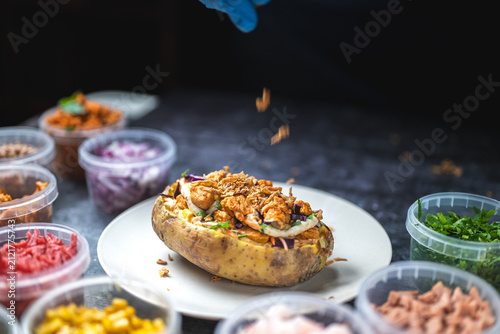 Baked potatoes with cheese, herbs, meat and butter. Copy space background. BBQ or steakhouse side dish favorite with tomato beans, cheddar cheese, bacon.