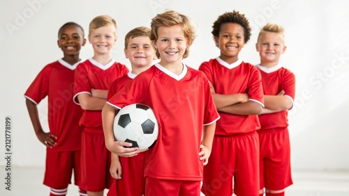 A group of young boys in red soccer uniforms stand together. One boy holds a soccer ball. They display smiles and confidence, showcasing teamwork and sportsmanship.