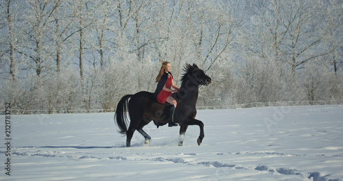 Woman riding black horse in snowy winter landscape