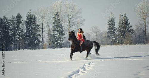 Woman riding black horse galloping in winter snow field