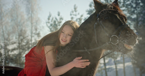 Woman in red dress hugging horse in winter forest