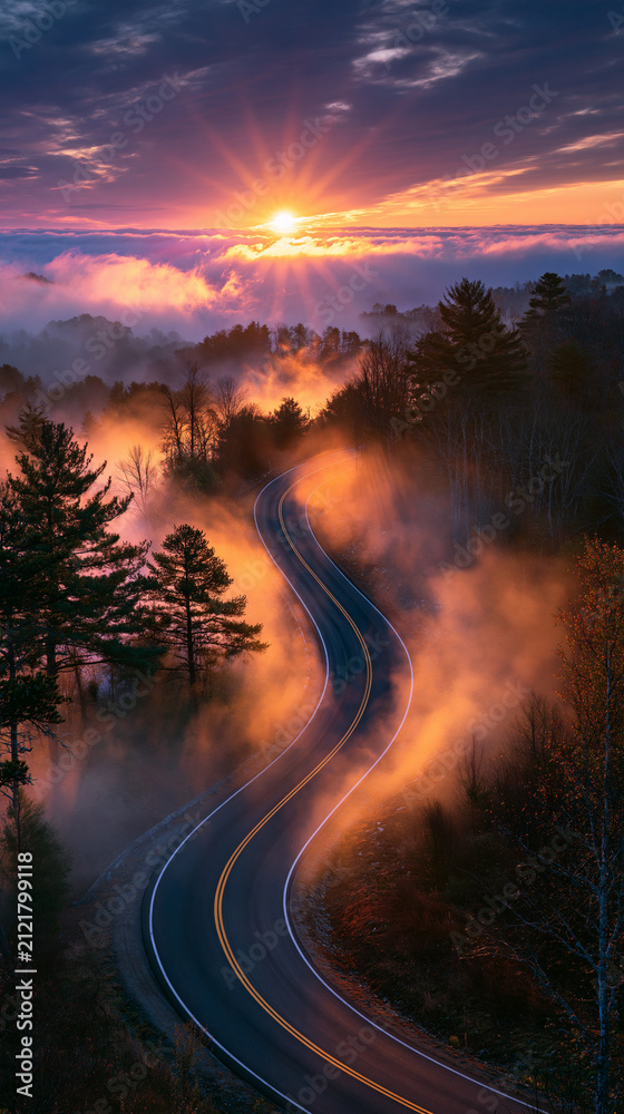 Obraz premium misty road emerging into sunrise light, serpentine asphalt through morning fog, ethereal dawn landscape with winding road