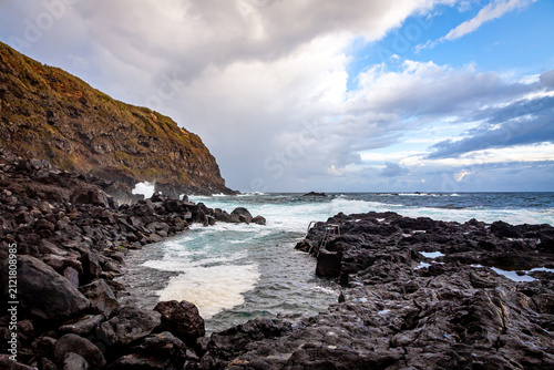 Scenic view of Ponta da Ferraria natural swimming area on Sao Miguel Island, Azores, Portugal, with rugged lava rocks, Atlantic waves and cloudy sky