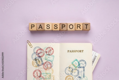 Flat lay travel concept with wooden block letters spelling passport and open passport with stamps on purple background