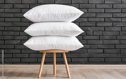Pile of soft bed pillows on chair near brick wall with space for text