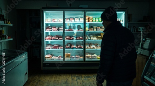 Person standing before bright illuminated grocery store refrigerated display
