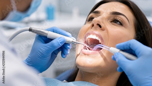 Close-up of dentist working on patient's teeth with dental drill and suction tube.