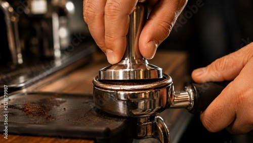 Close-up of barista hands pressing coffee grounds with a tamper in a portafilter