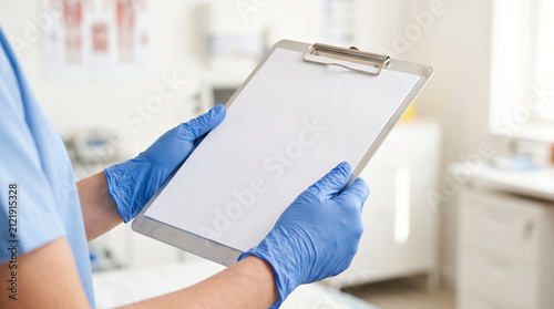 Doctor wearing blue gloves holding blank medical clipboard in clinic