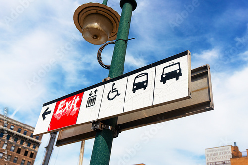 Fotografie A weathered urban wayfinding sign featuring icons for elevators, accessibility, buses, and taxis, captured against a bright, minimalist sky to represent modern city infrastructure
