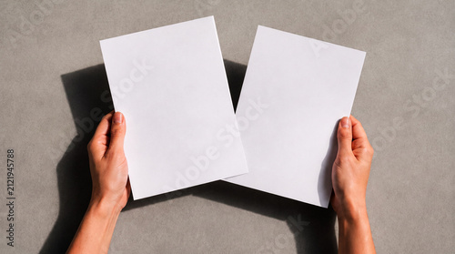 Person holding two blank white sheets of paper for mockup