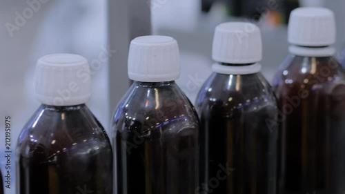 Conveyor belt of bottle shrink sleeve labeling machine with empty amber glass bottles at plastic packaging exhibition or factory - production line: demonstration mode, close up view