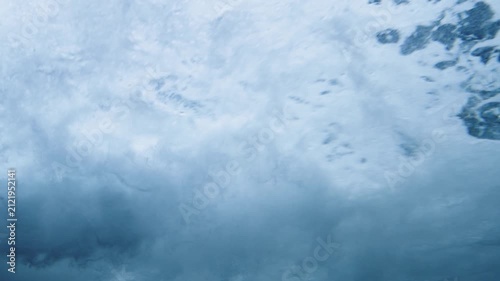 Dramatic underwater shot of turbulent ocean waves breaking with white foam and swirling air bubbles. Dynamic water movement creating a beautiful abstract background pattern in the deep blue sea.
