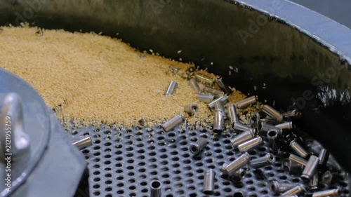Vibratory finishing round bowl machine uses abrasive particles for polishing and cleaning metal details - close up view. Metalworking, industrial, equipment and manufacturing concept