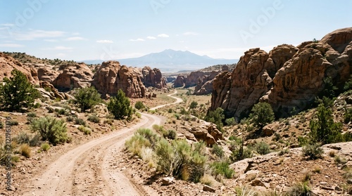 A scenic dirt road winds through a rugged desert landscape with rocky formations and distant mountains under a clear sky