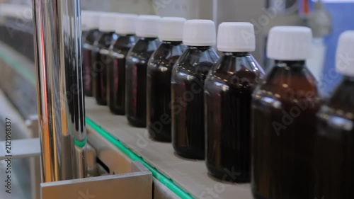 Close up view: row of moving empty amber glass bottles on conveyor belt. Production line, demonstration mode of bottle shrink sleeve labeling machine at plastic packaging exhibition, plant, factory