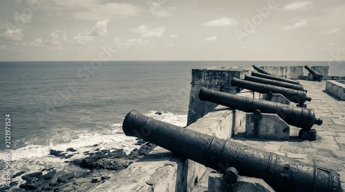 A powerful and historically significant image of the gun battery at Cape Coast Castle in Ghana West Africa. The photograph shows old colonial artillery cannons aimed out towards the vast Atlantic