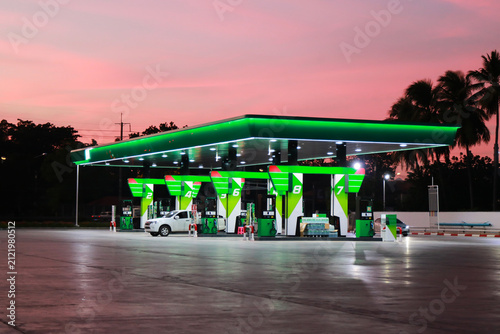 Modern green gas station glowing under a pink sunset sky at dusk.