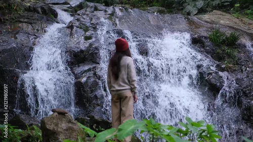 Blurred rear view of a woman looking at the waterfall in the forest