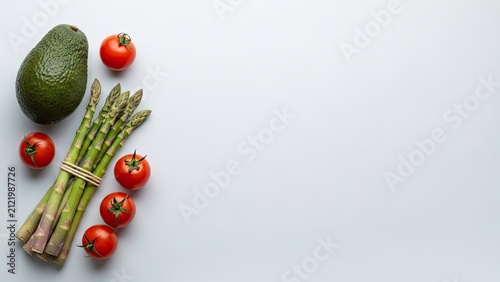 Fresh avocado asparagus and cherry tomatoes arranged on light background