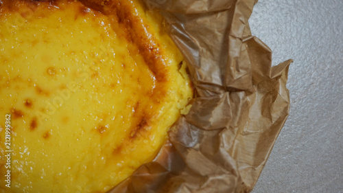 Obraz na plátně Close-up of a freshly baked Basque burnt cheesecake with a golden caramelized crust, wrapped in rustic brown parchment paper on a grey stone background