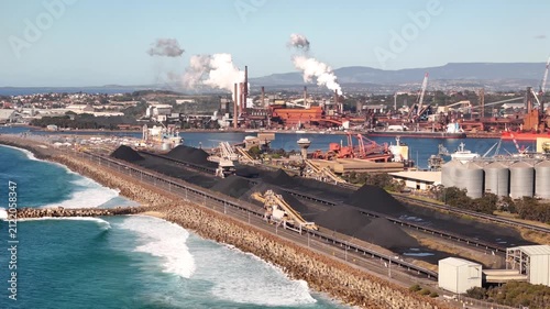 Aerial drone view of Port Kembla, Illawarra Region, NSW, Australia showing visible plumes rising from industrial chimneys, the seaport, industrial complex and small harbour foreshore in August 2026   