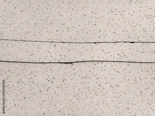 Long horizontal cracks on a speckled light gray ceramic tile surface.