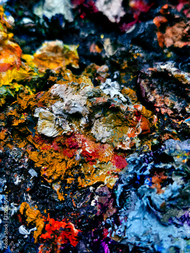 Vibrant messy artist palette covered in glossy paint, scattered brushes and tubes, dried paint