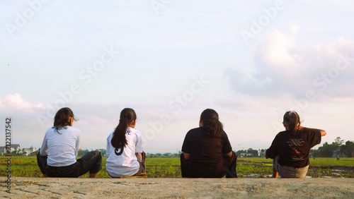 Group of young women sitting together and looking at the rural landscape at sunset.
