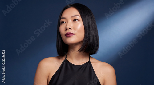 Portrait of young asian woman wearing black spaghetti strap top on dark blue