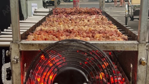 Close-up of rotating meat skewers grilling over glowing charcoal at a Vietnamese street food stall. A fan blows air onto the coals to maintain high heat during traditional barbecue cooking.