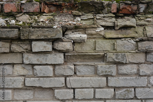 A light gray wall, an old building, a fence with green moss and moisture. Light gray, red bricks, beautiful, stylish brickwork.