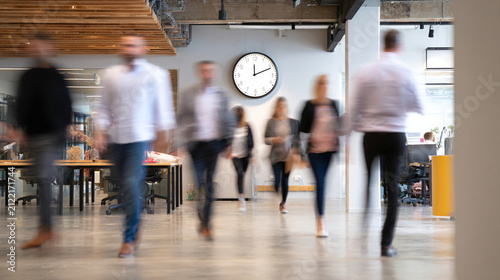 Professional people walking through modern office hallway blurred in motion during a busy workday afternoon setting