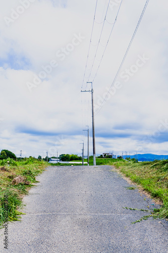 Rural road with utility poles and power lines under a cloudy summer sky in Japan