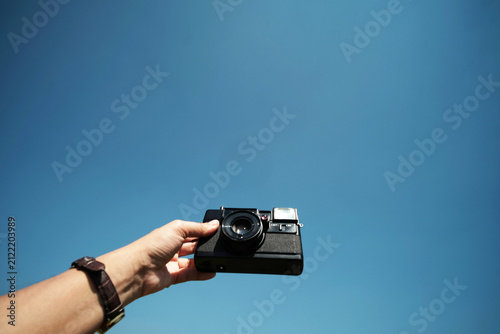 Close up woman hand holding vintage black film camera with blue sky with sunny day. Copy space