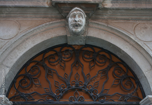 Head of man with mustache, arch keystone, decorative architectural, openwork metal grille. Koper, Slovenia.